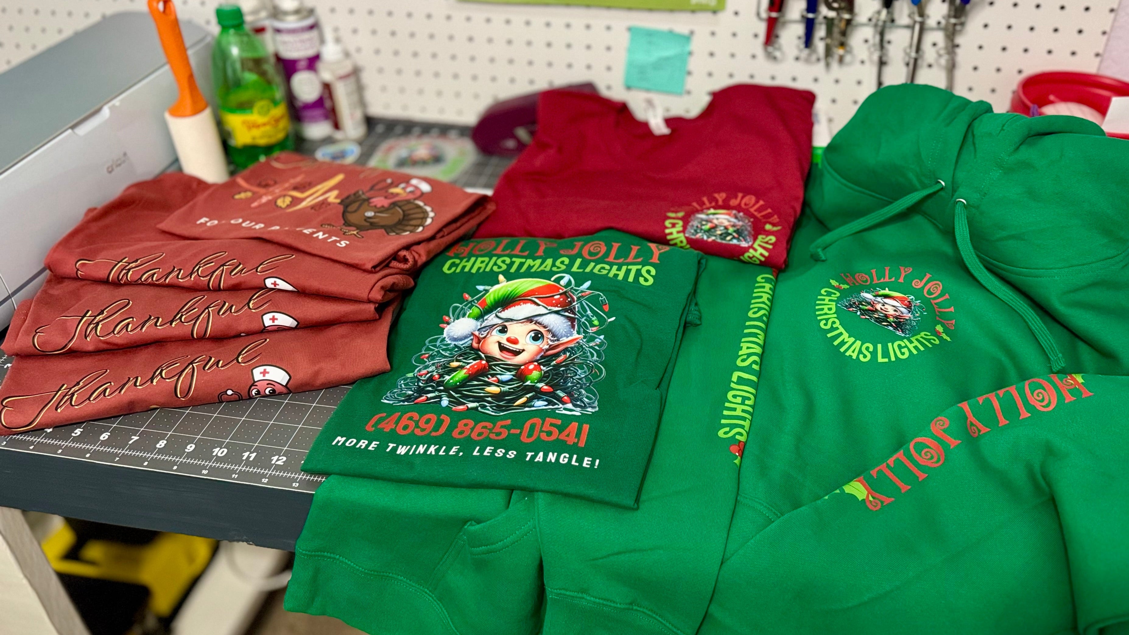 Green hoodies with festive designs on a workbench in a workshop setting.